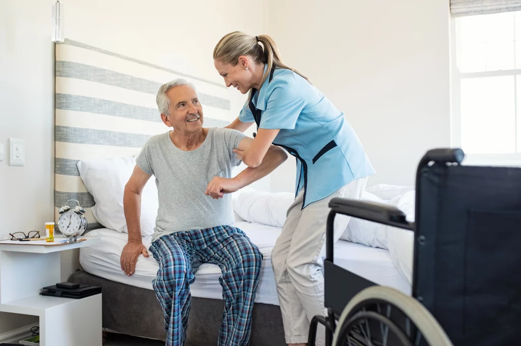 Pflegekraft unterstützt älteren Mann beim Aufstehen aus dem Bett – Mobilitätshilfe im Rahmen der häuslichen Pflege